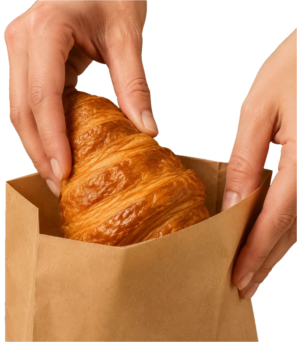 Unas manos guardan un cruasán en una bolsa de papel kraft